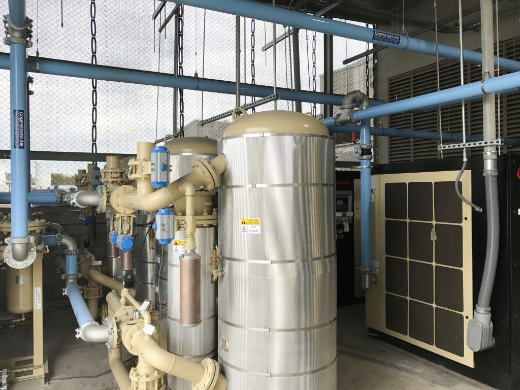 Industrial water filtration system with pipes, valves, and tanks in a utility room, serviced by Air Centers of Florida.