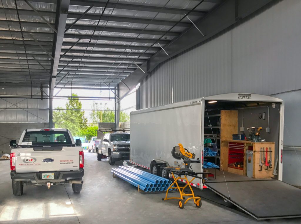 A well-equipped mobile workshop inside a large enclosed trailer with the door open, parked inside a spacious Air Centers of Florida industrial garage, alongside a white pickup truck.