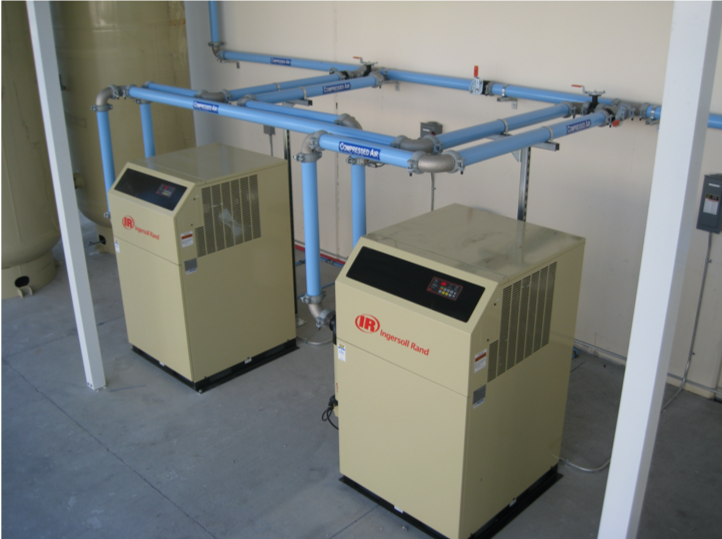 Two industrial air compressors from Air Centers of Florida installed in a utility room with overhead piping.