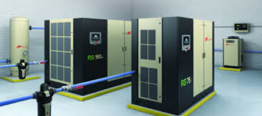 Modern industrial room with high-capacity air compressors and a centralized compressed air system by Air Centers of Florida, featuring large black and gray units connected by blue and yellow pipes.