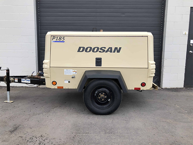 A portable Doosan p185 air compressor on a single-axle trailer, provided by Air Centers of Florida, is parked in front of an industrial garage door.