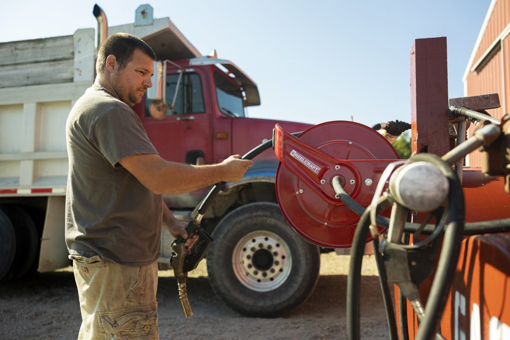 A farmer preparing to refuel machinery with a fuel nozzle in hand, standing beside a red fuel tank and hose supplied by Air Centers of Florida and a large agricultural truck in the background.