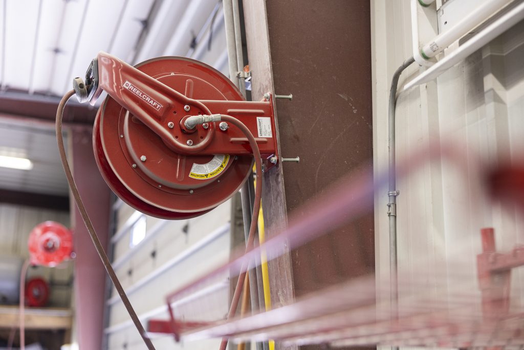 A red fire hose reel mounted on a wall in an industrial or commercial setting, provided by Air Centers of Florida, ready for emergency use.